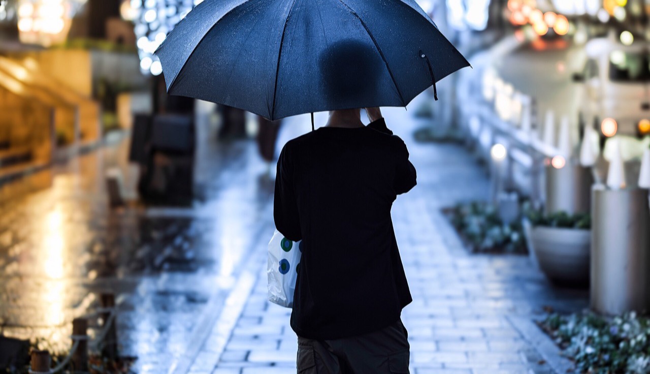 A figure under an umbrella on a wet, lamp-lit Tokyo street.