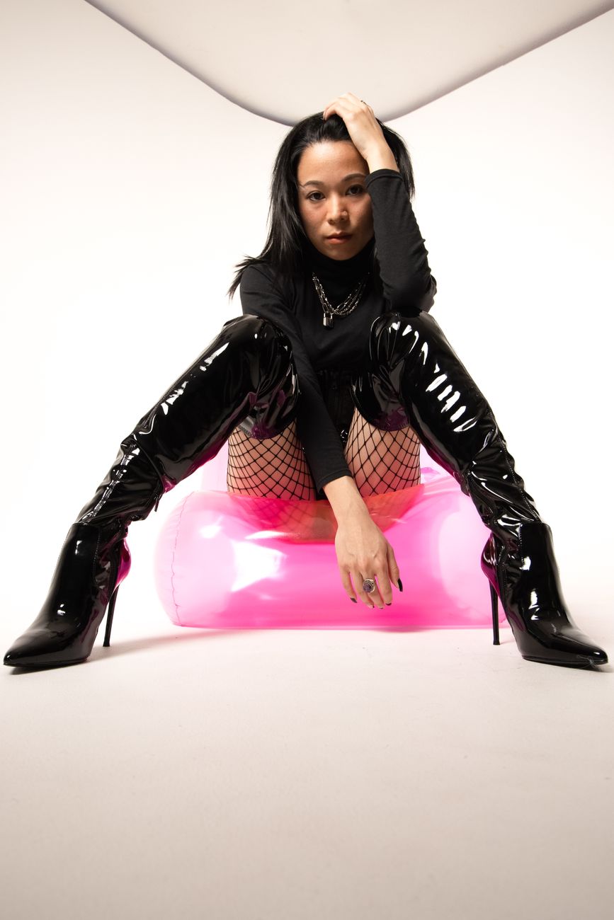 Model in a black latex outfit and thigh-high boots lounging on a hot-pink inflatable