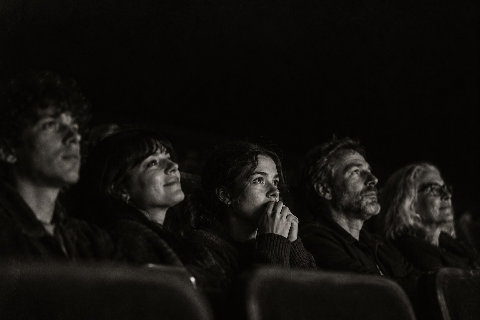 A row of audience faces lit by the screen