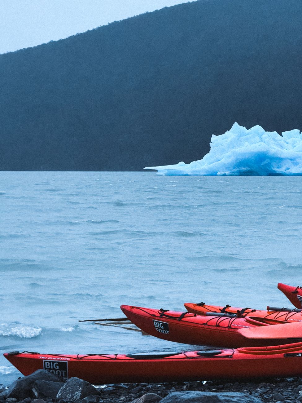 A kayaker paddling beneath a towering glacier wall