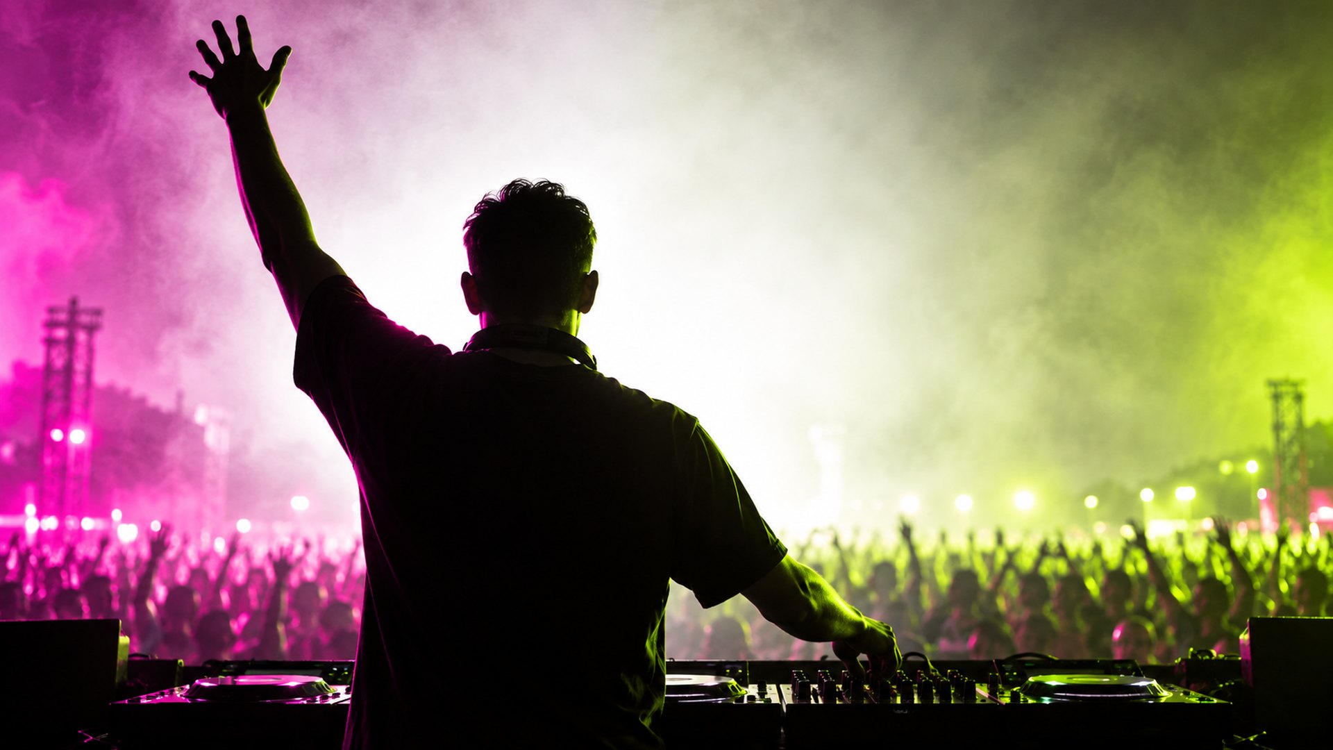 A DJ seen from behind, backlit by a wall of white light, arms raised over the decks