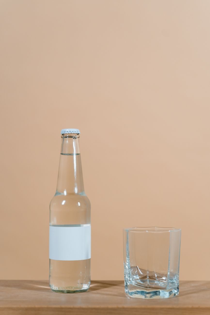 A clear glass bottle with a blank label beside an empty tumbler