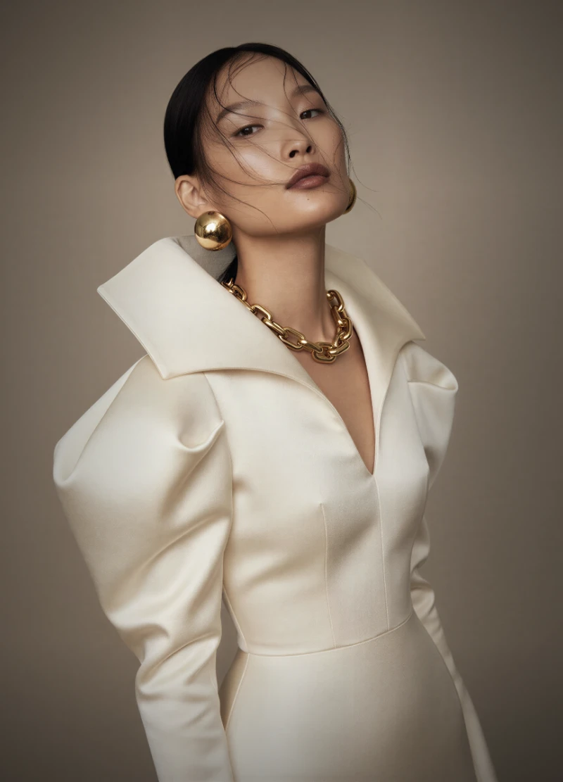 Cream structured dress with a wide portrait collar, against a warm taupe ground