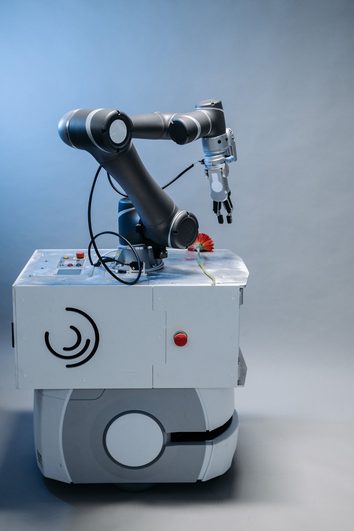 A dark six-axis robot arm with a gripper mounted on a white mobile base against a grey backdrop