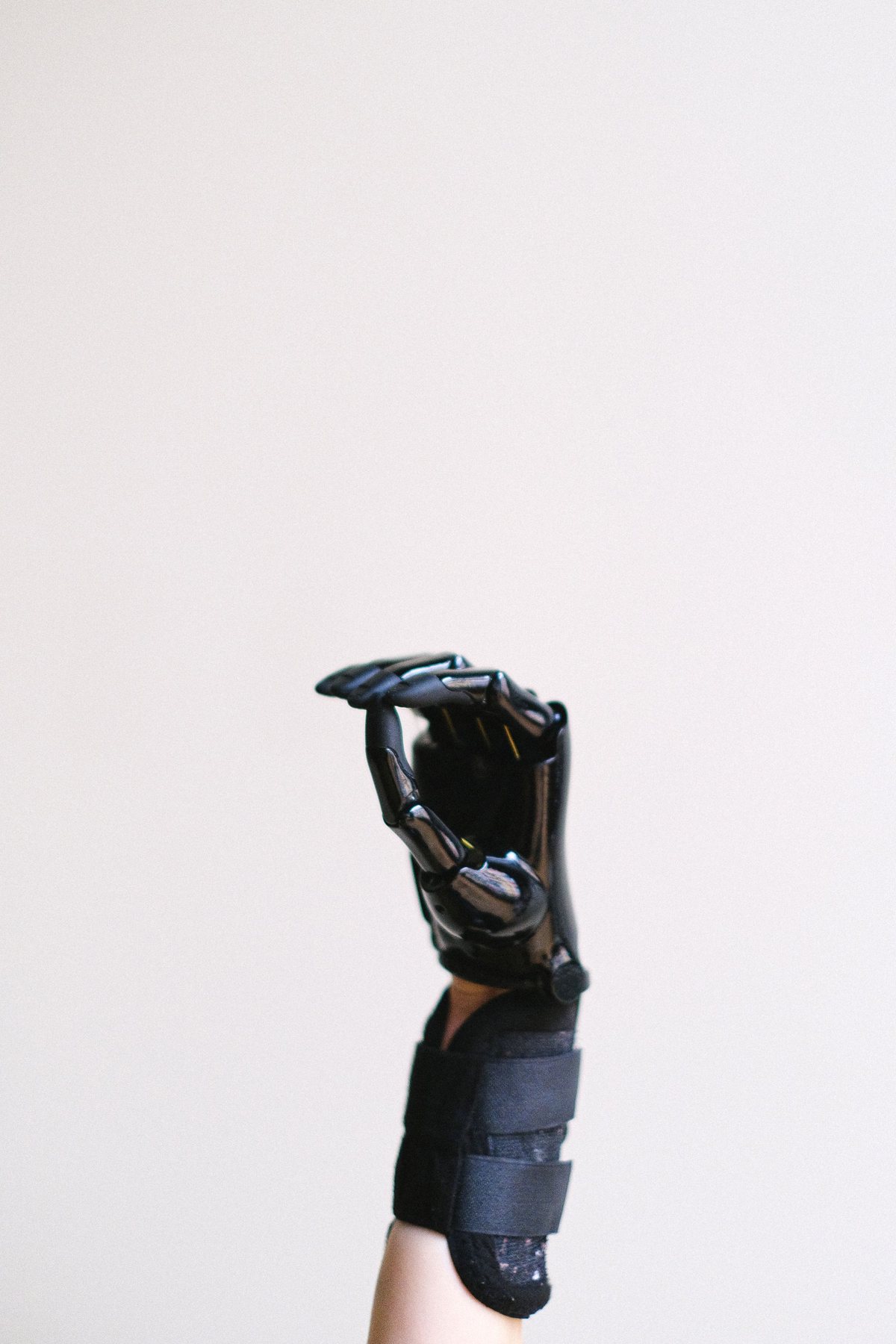 A raised hand wearing a black articulated exoskeleton glove against a plain white wall