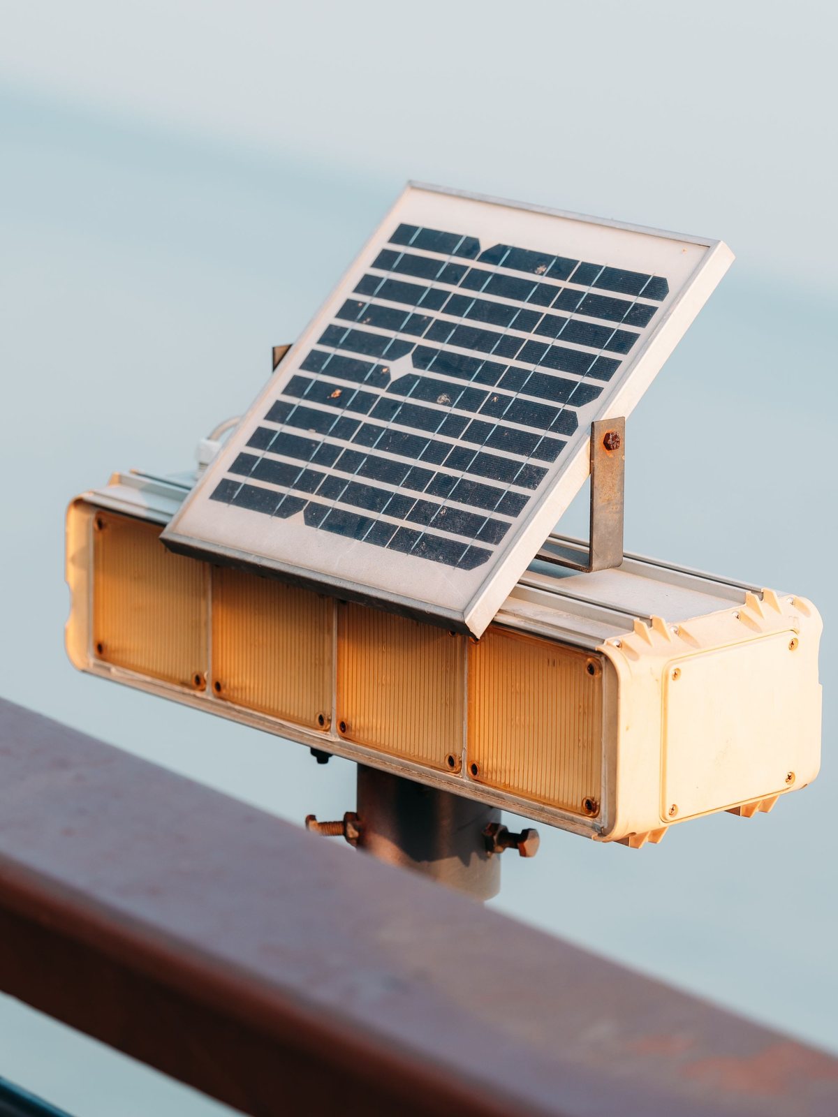 A compact solar panel on top of an amber signal beacon fixed to a railing