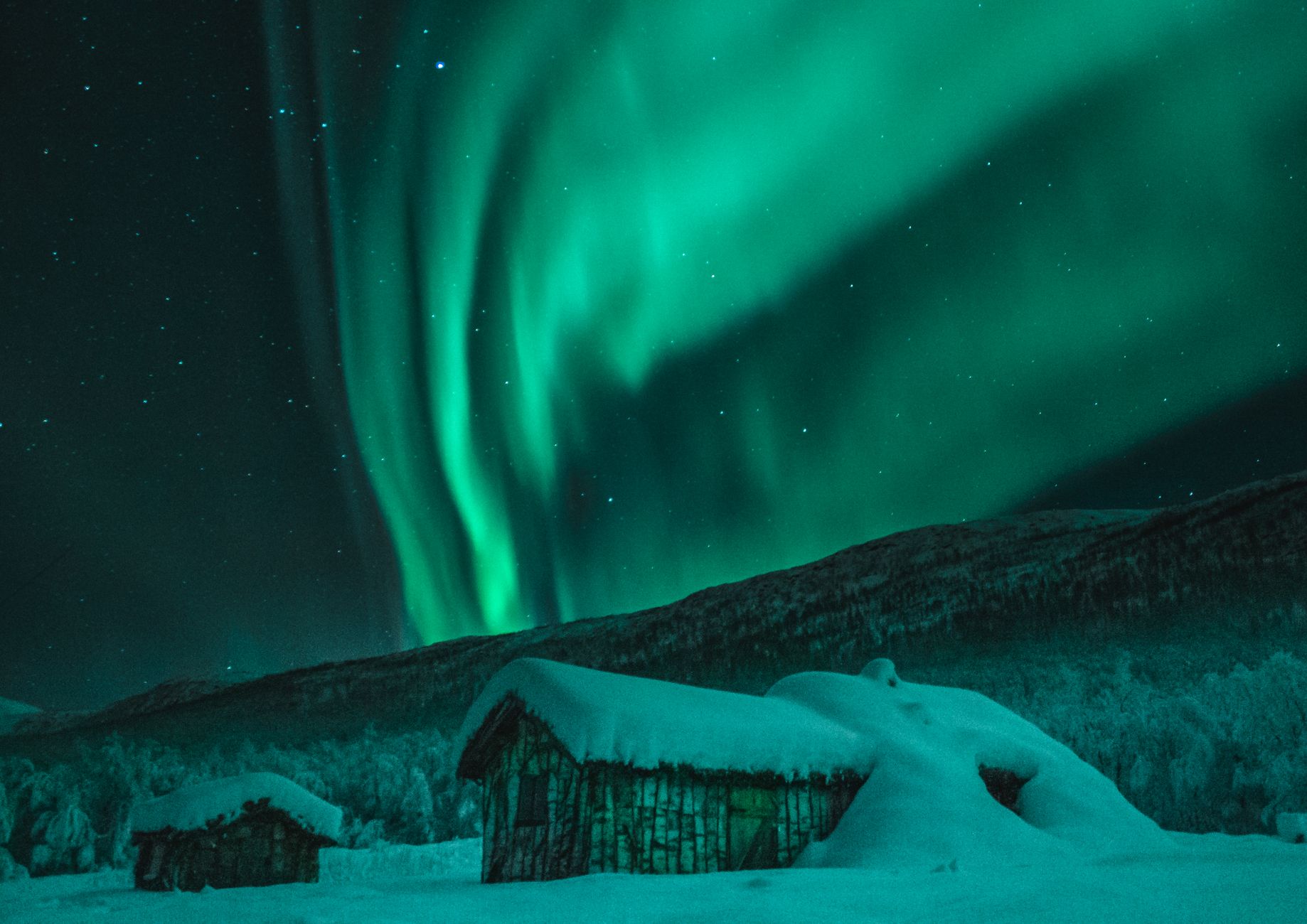 Green aurora ribbons over a snowy valley at night