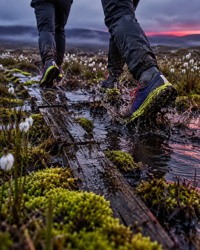 Two pairs of muddy shoes splashing along a sunken boardwalk across a bog