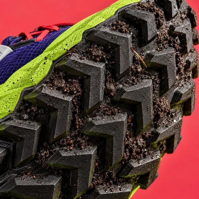 Black chevron outsole lugs with crumbs of wet earth, on red