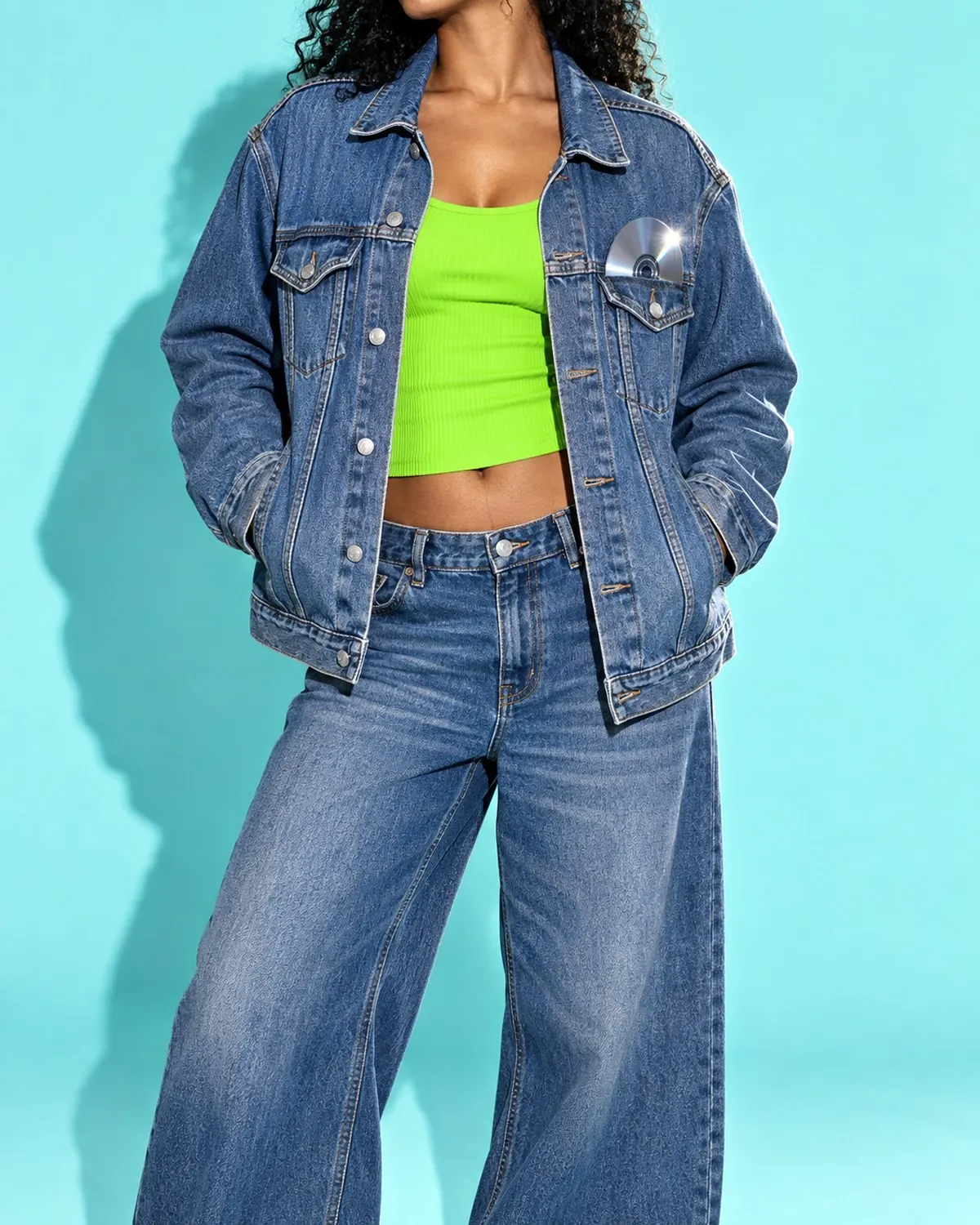 Oversized denim trucker jacket over a slime-green tank on aqua paper