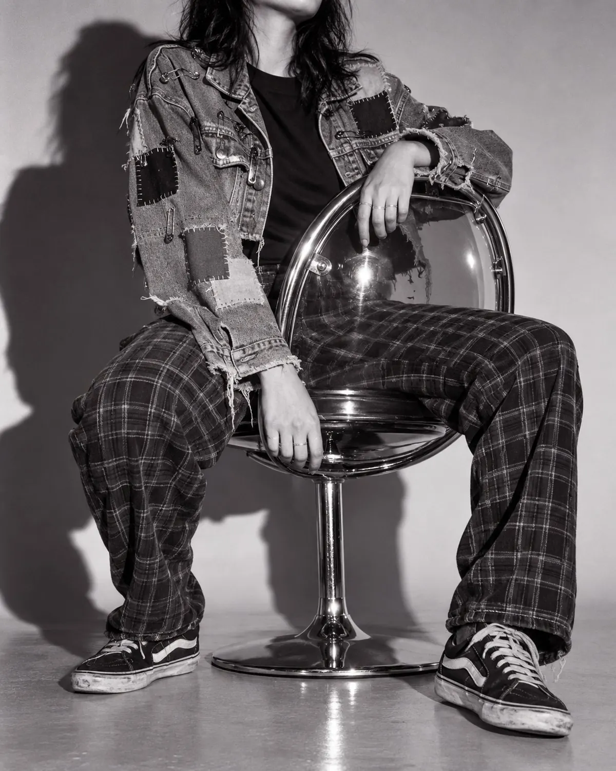 The same jacket cropped, pinned and patched, worn backwards on a chrome bubble chair