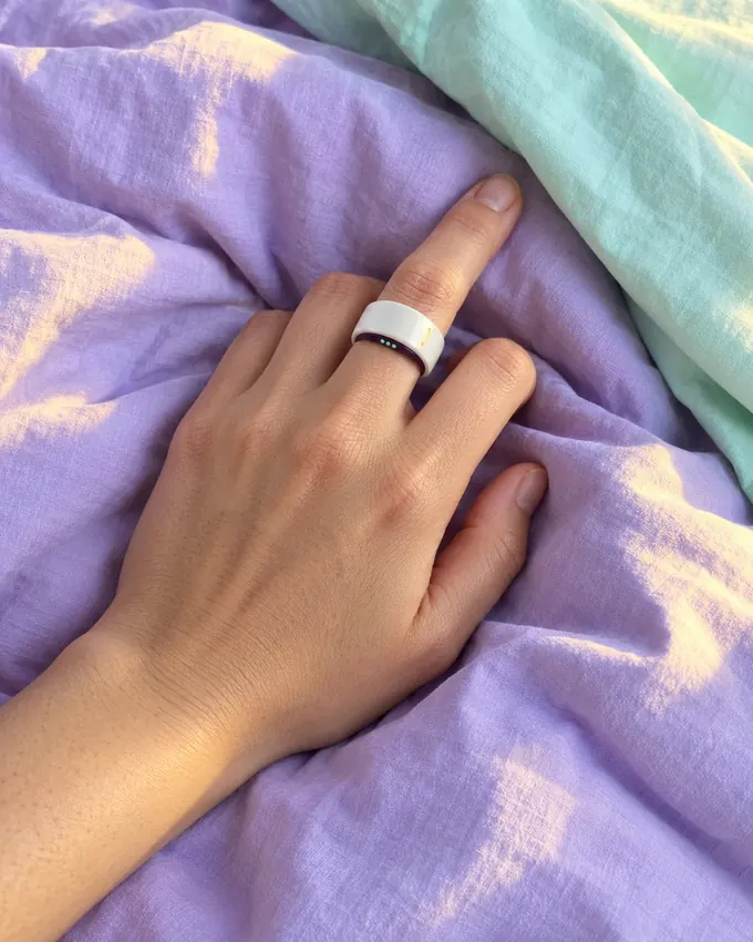 A hand resting on a lilac duvet, wearing a white ceramic ring