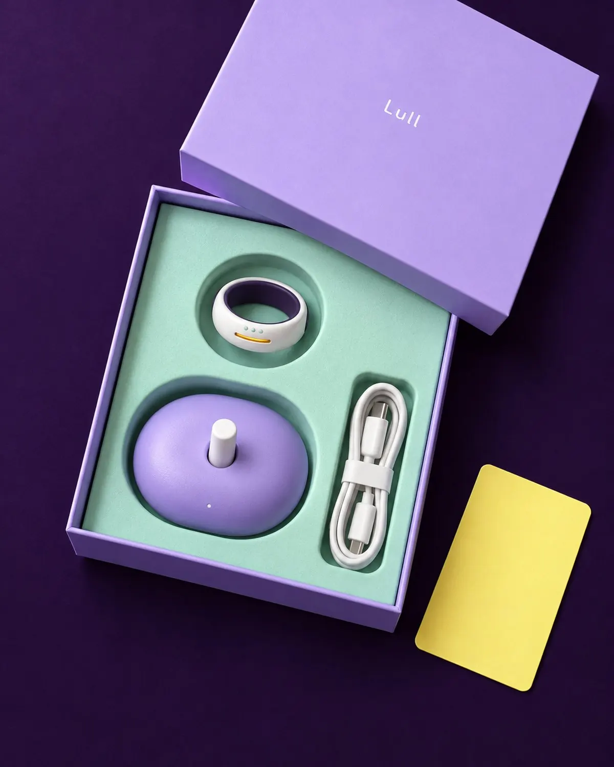 The Lull box opened on a plum surface: ring, pebble dock and a short cable