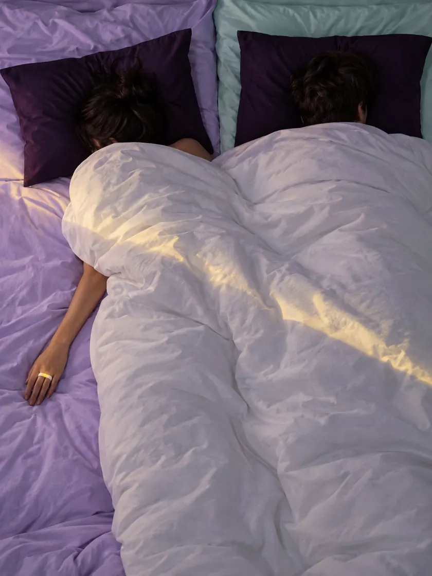 A colour-blocked bed from above, lilac and mint sheets, two sleepers under a duvet
