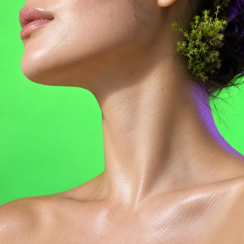 A calm, glowing jawline in profile with a sprig of moss tucked behind it