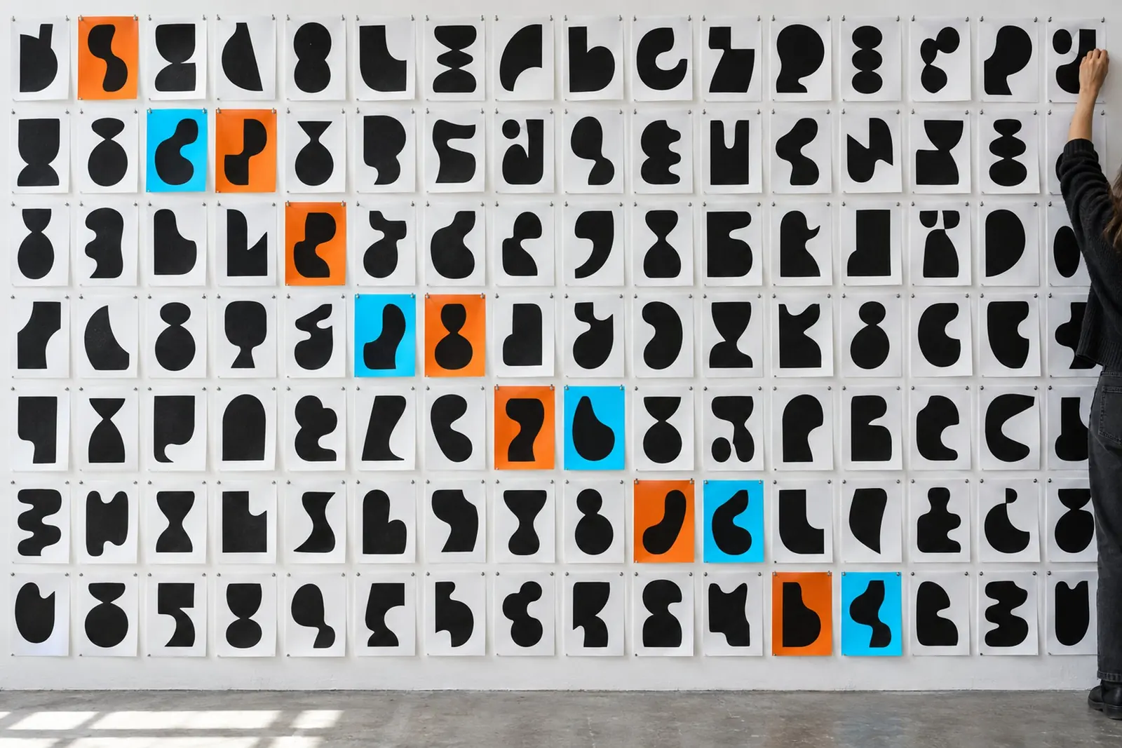 A white wall covered edge to edge in pinned black type specimens with a few orange and cyan sheets