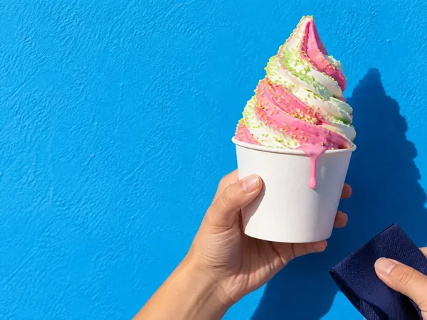 Hand holding a pink and white soft-serve against a blue wall