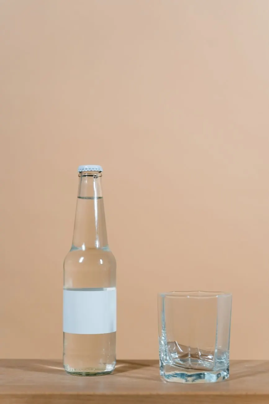 A clear glass bottle with a blank label beside an empty tumbler
