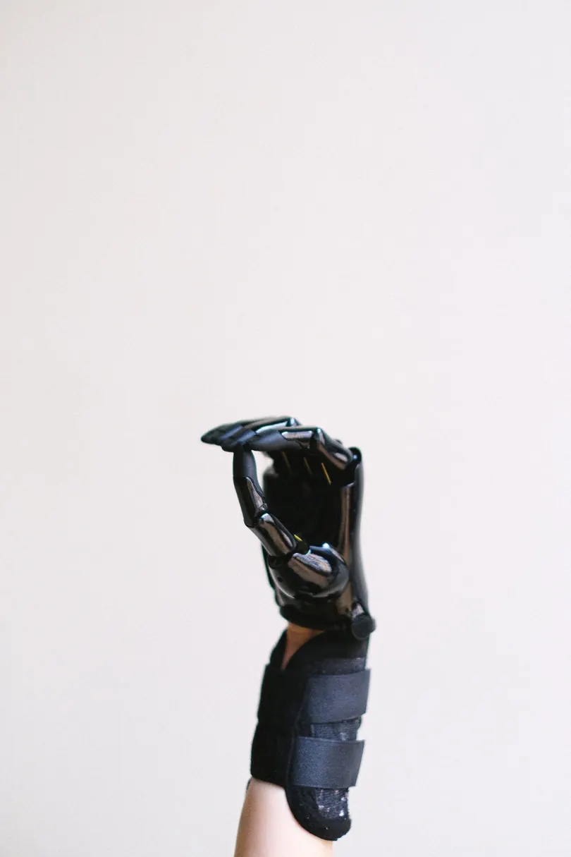 A raised hand wearing a black articulated exoskeleton glove against a plain white wall