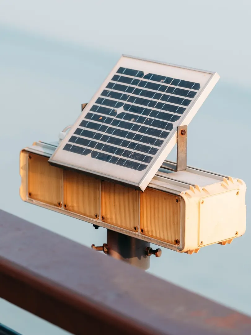 A compact solar panel on top of an amber signal beacon fixed to a railing