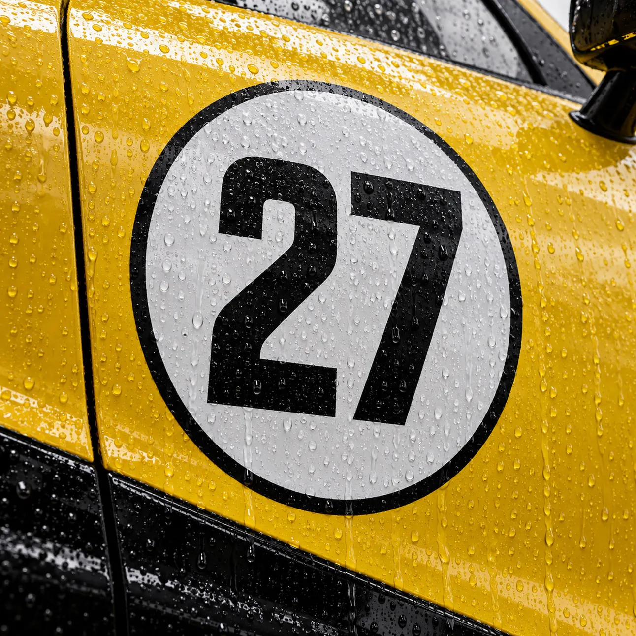 Close-up of the white number 27 roundel on the car's door, rain beads on the paint